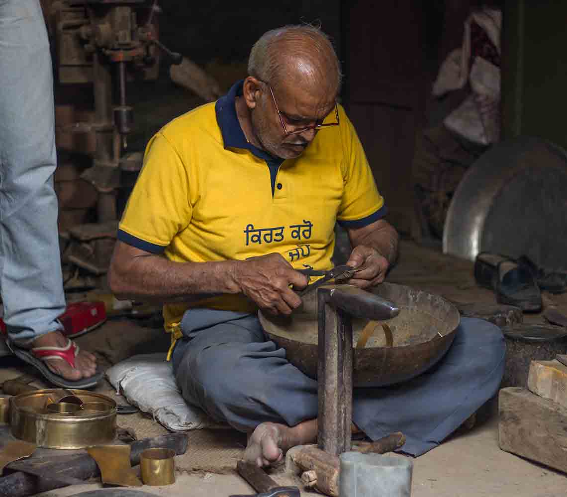 An artisan working on a copper article using handheld tools