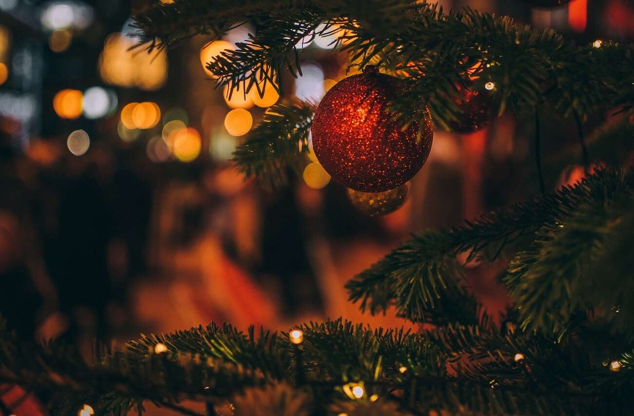 A red shiny bauble hanging from a Christmas tree