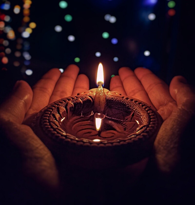 Pair of hands holding a diya with lights in the background
