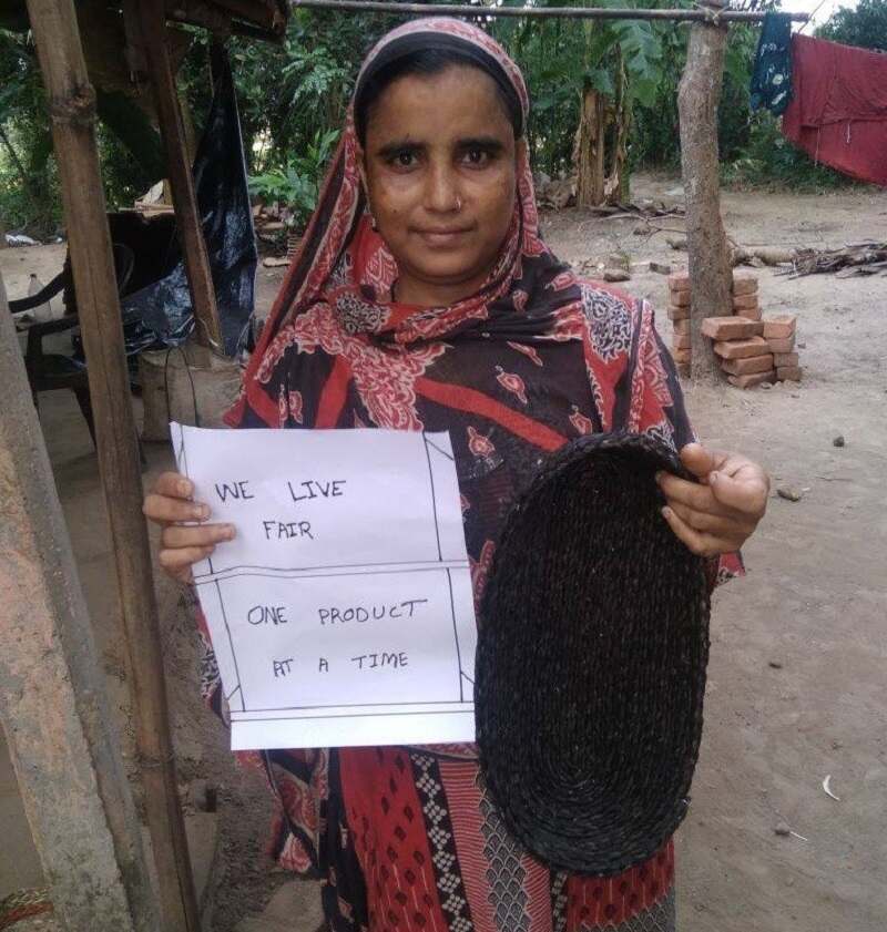 A rural woman artisan holding a signage that reads "We live fair. One product at a time"