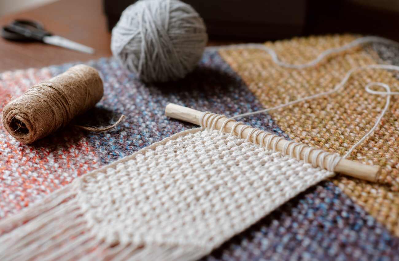 A macrame hanging work in progress with yarns balls on the table