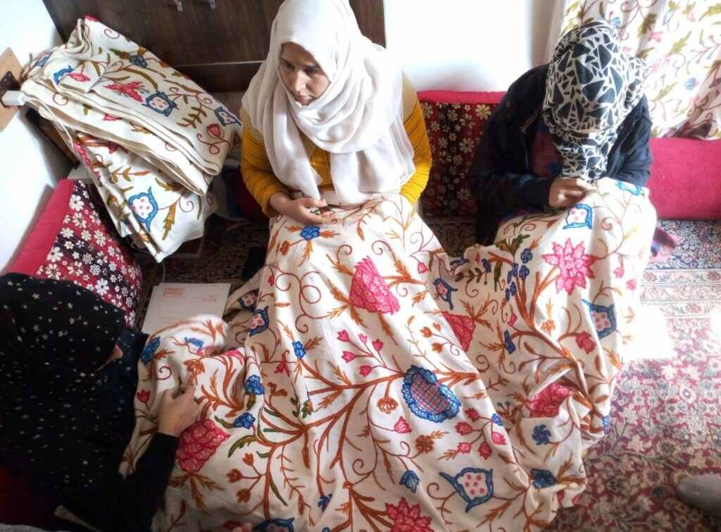 Three women artisans embellishing a piece of fabric with embroidery