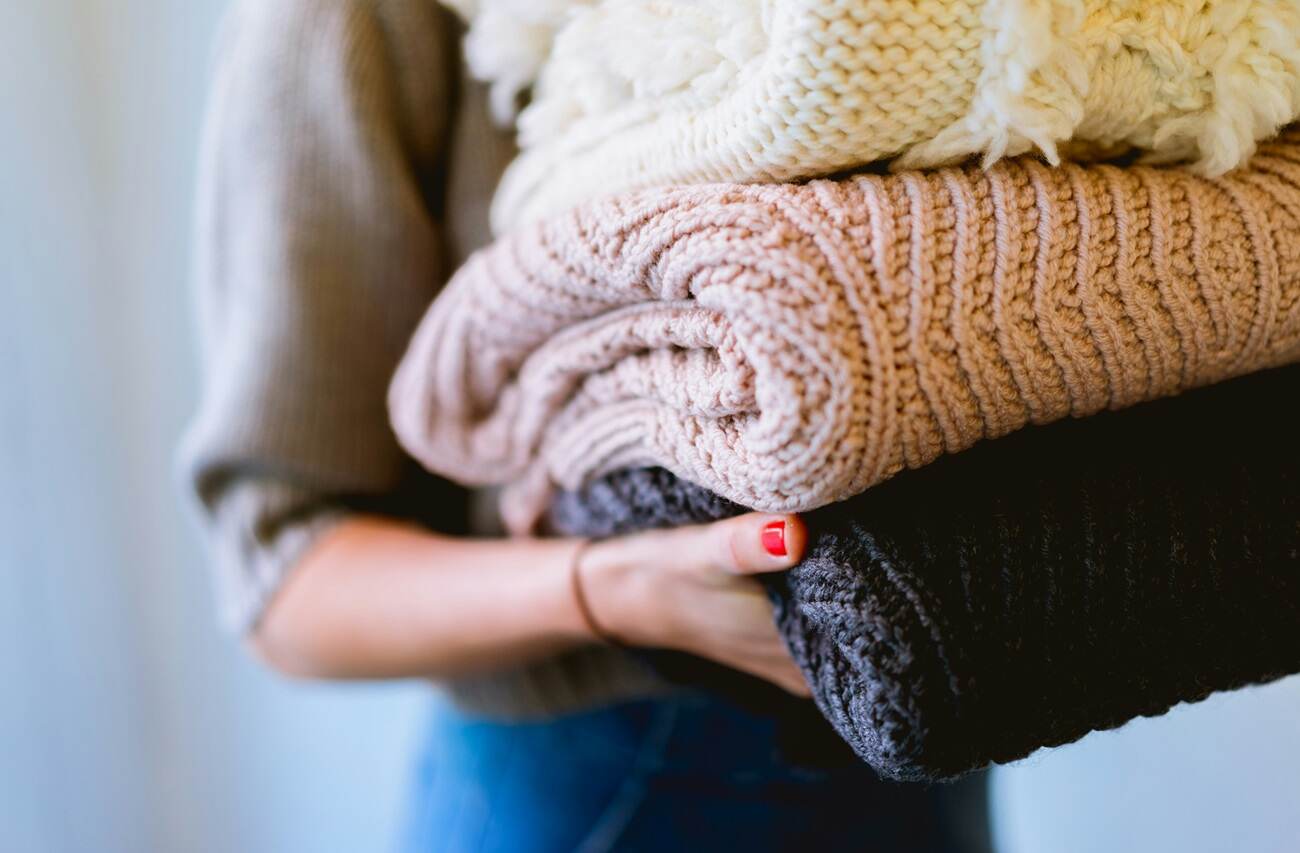 A woman holding neatly folded sweaters